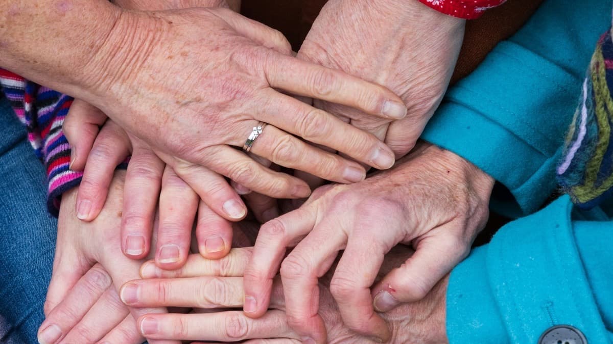 Several pairs of hands of different ages stacked on top of one another, sleeves in bright knits and prints.