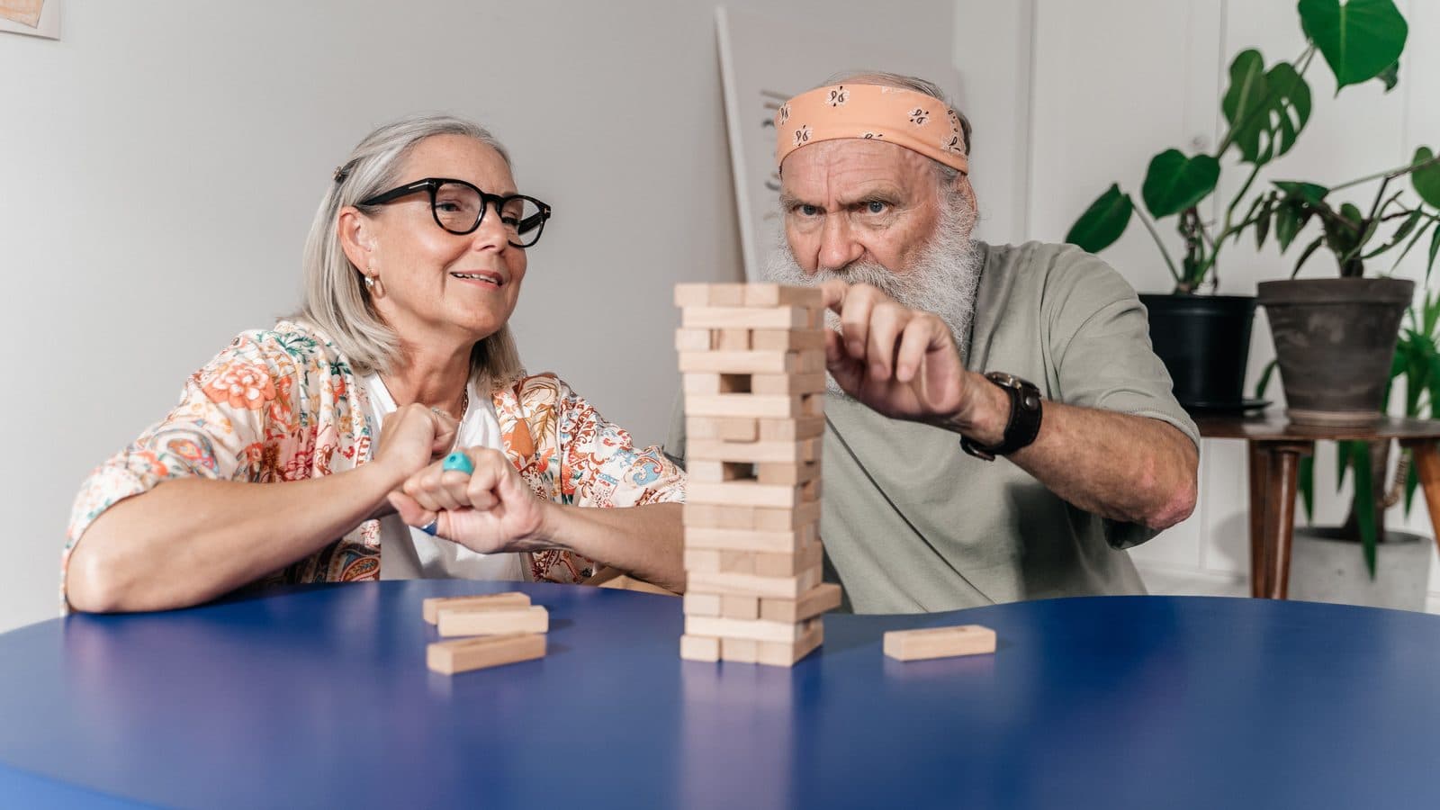 Two older people playing a tower-block game together at a table.