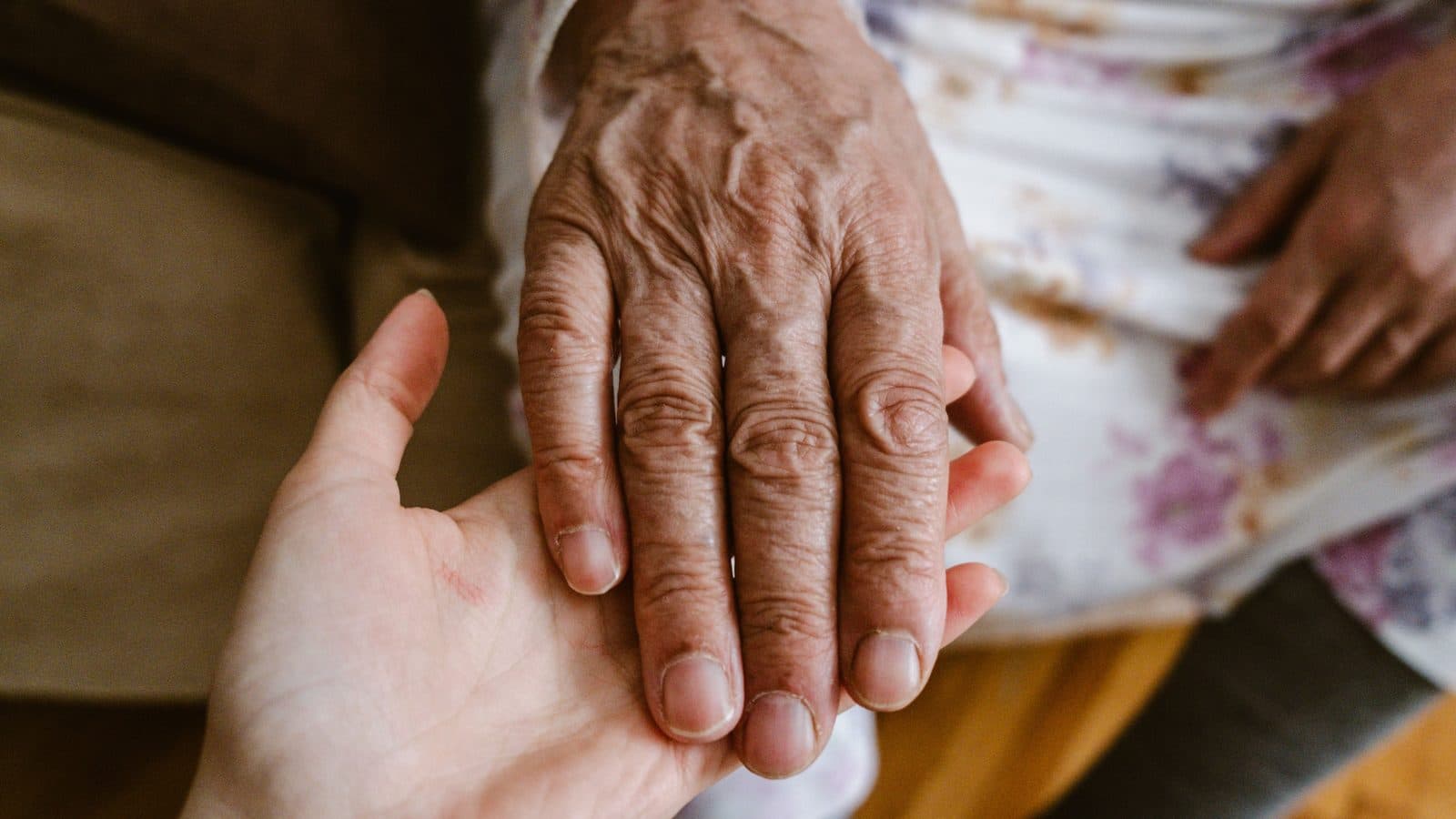 A younger hand resting on an older woman's hand.